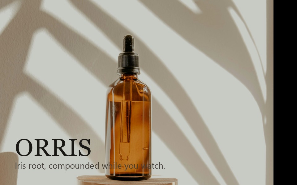 ORRIS: amber dropper bottle on a pale wall with leaf shadow, iris perfume house.