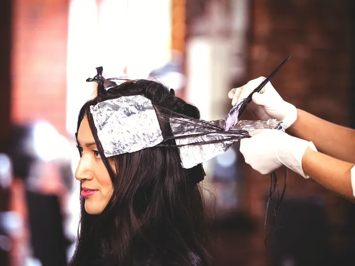 A colourist applying hair colour to foiled sections of a client's dark hair.