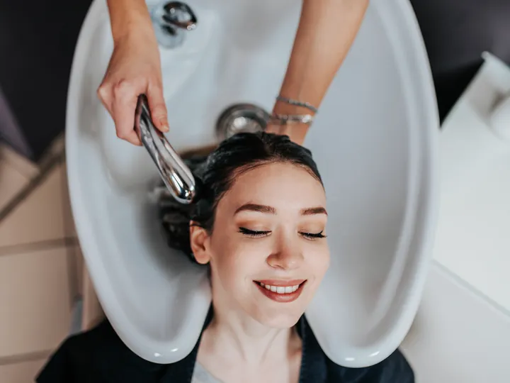 A client relaxing at the wash basin while a stylist rinses their hair.