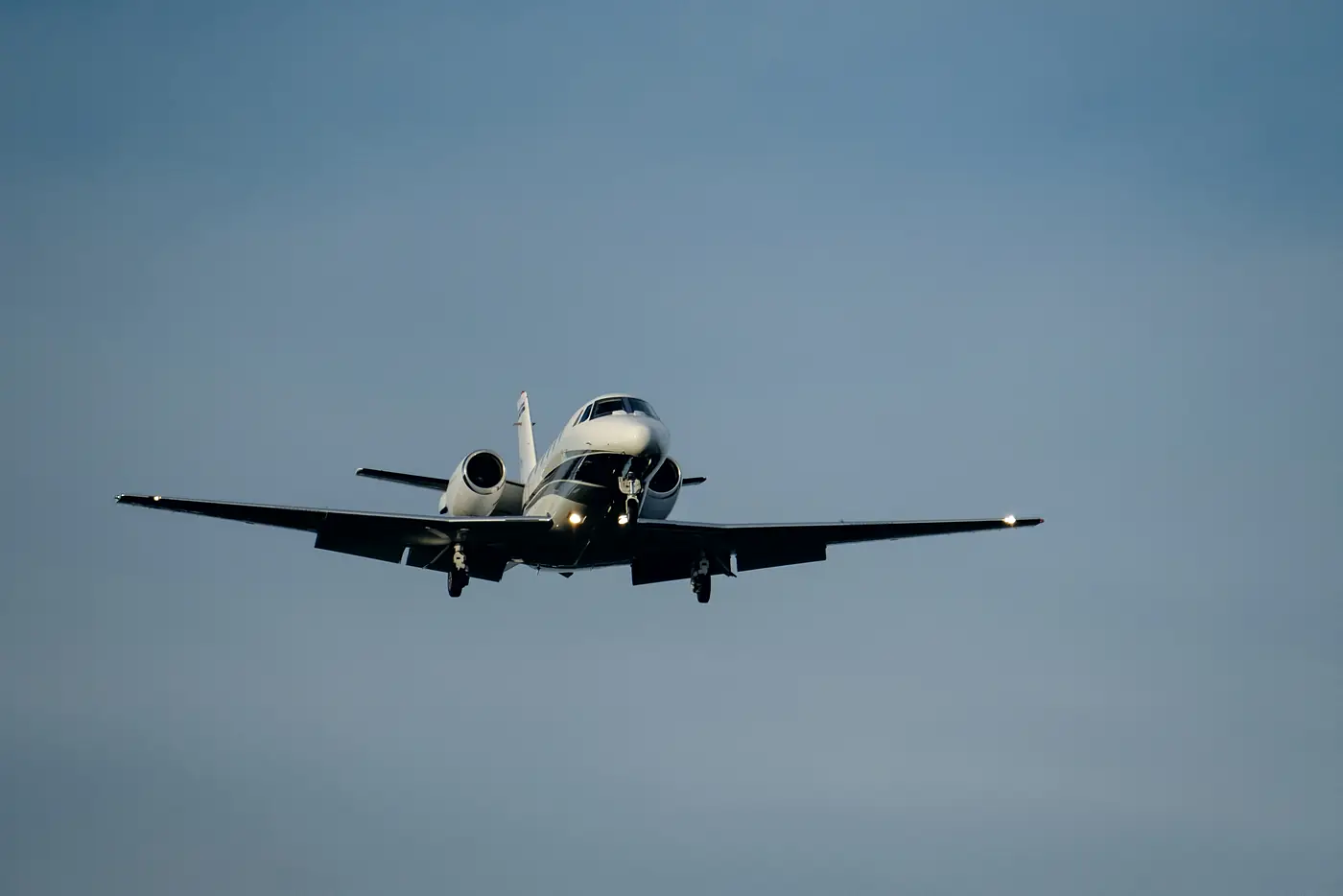 A business jet on final approach, landing lights on, against a clear sky.