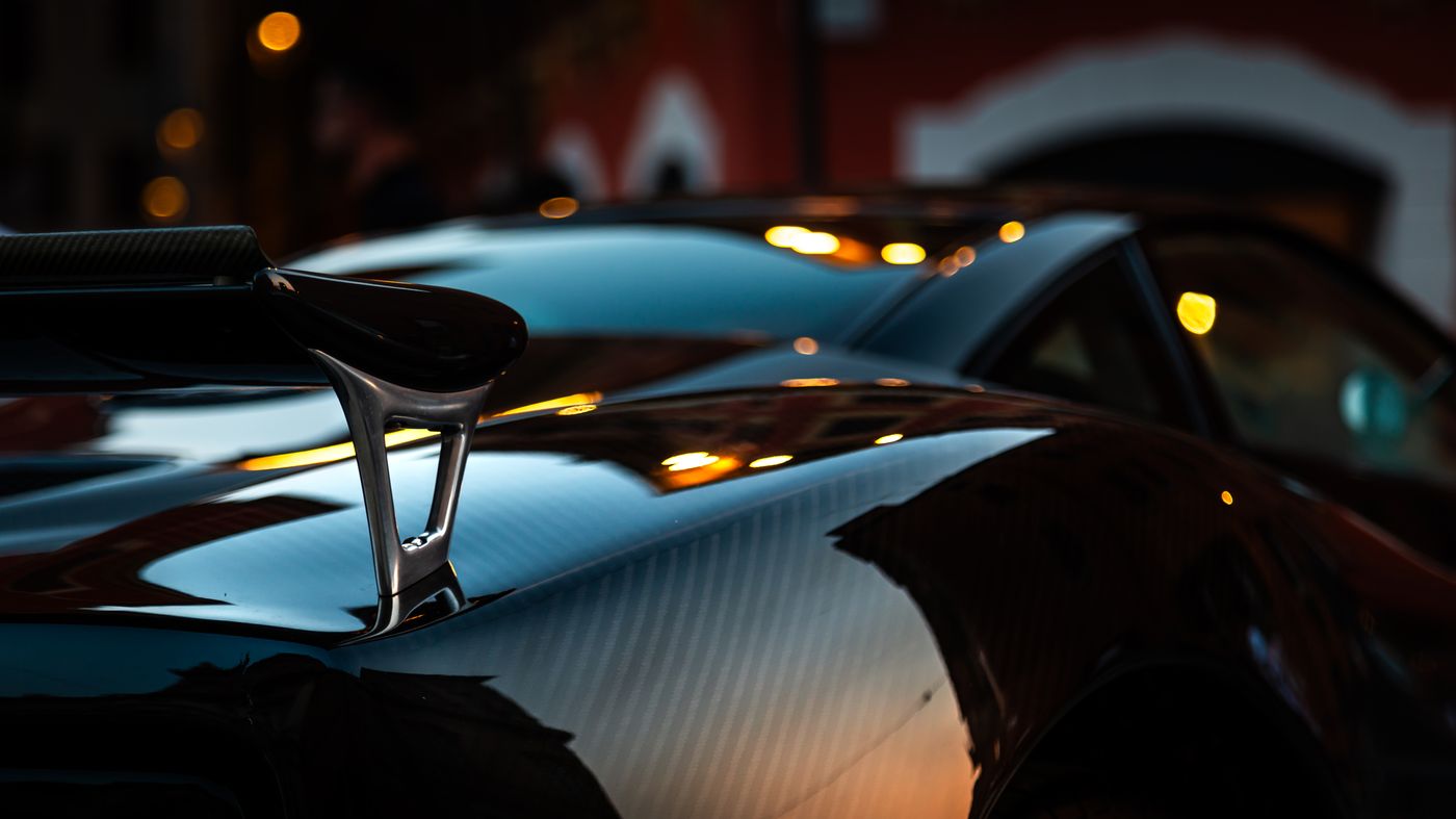 The rear wing and exposed carbon deck of the Aviator at dusk, reflections running along its edge.