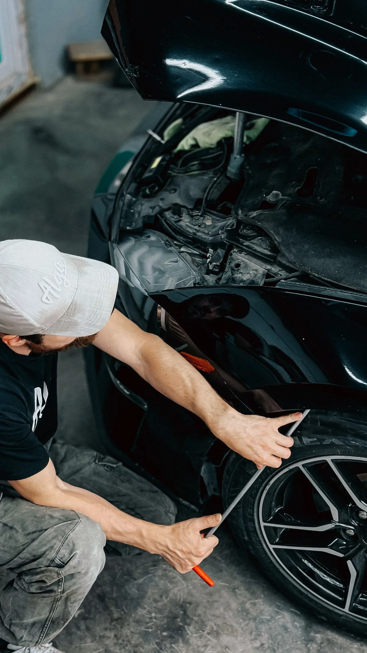 Technician assessing the front panel of a black car with the hood raised