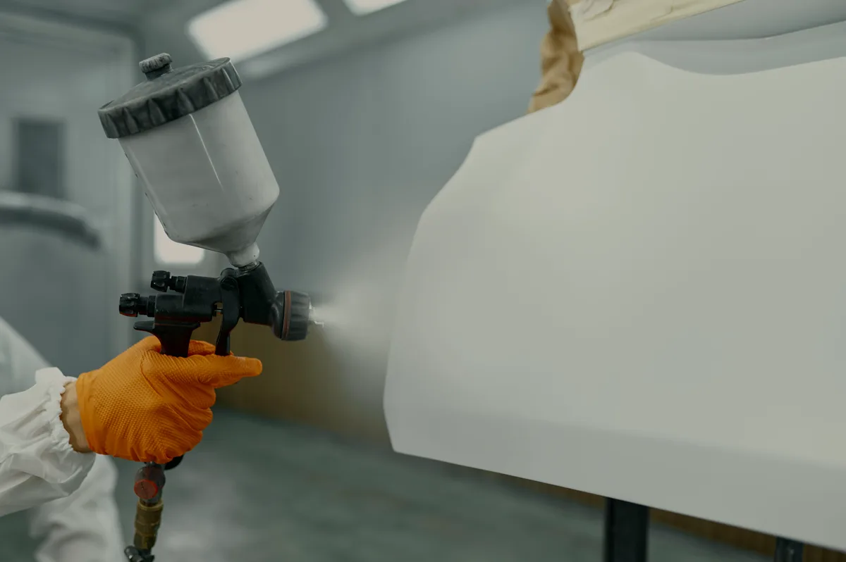 Spray gun laying paint onto a car panel in the booth