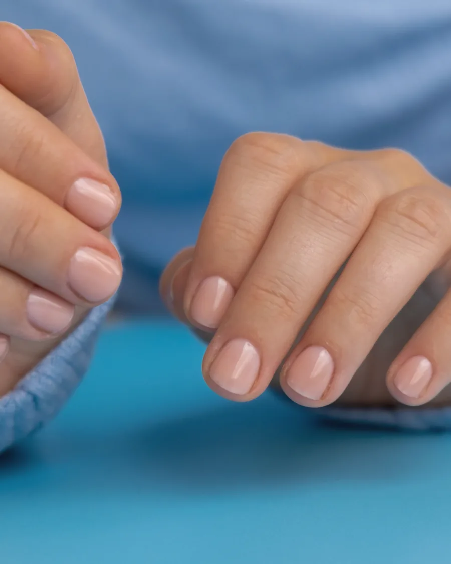 A pair of hands resting on a pale blue surface, nails finished in a soft natural pink.