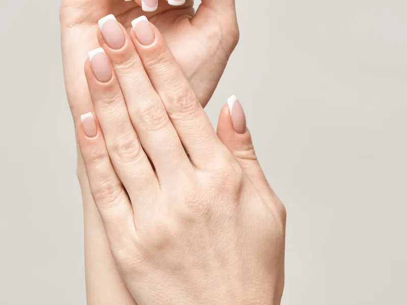 Two hands with a classic pale french manicure.