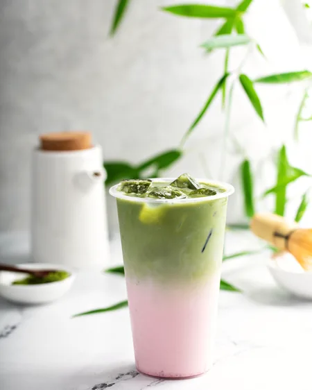 A tall glass layered pink and green — strawberry beneath iced matcha — on a marble counter.