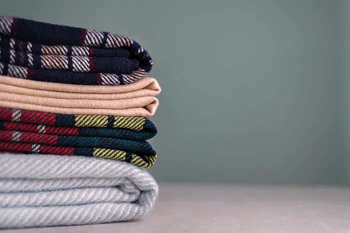 A stack of finished woollen blankets, folded, on a grey shelf.