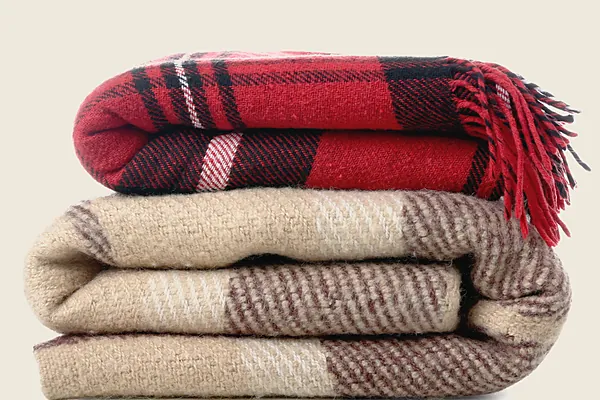 Two folded woollen blankets, a red tartan on a camel check, with fringed ends.