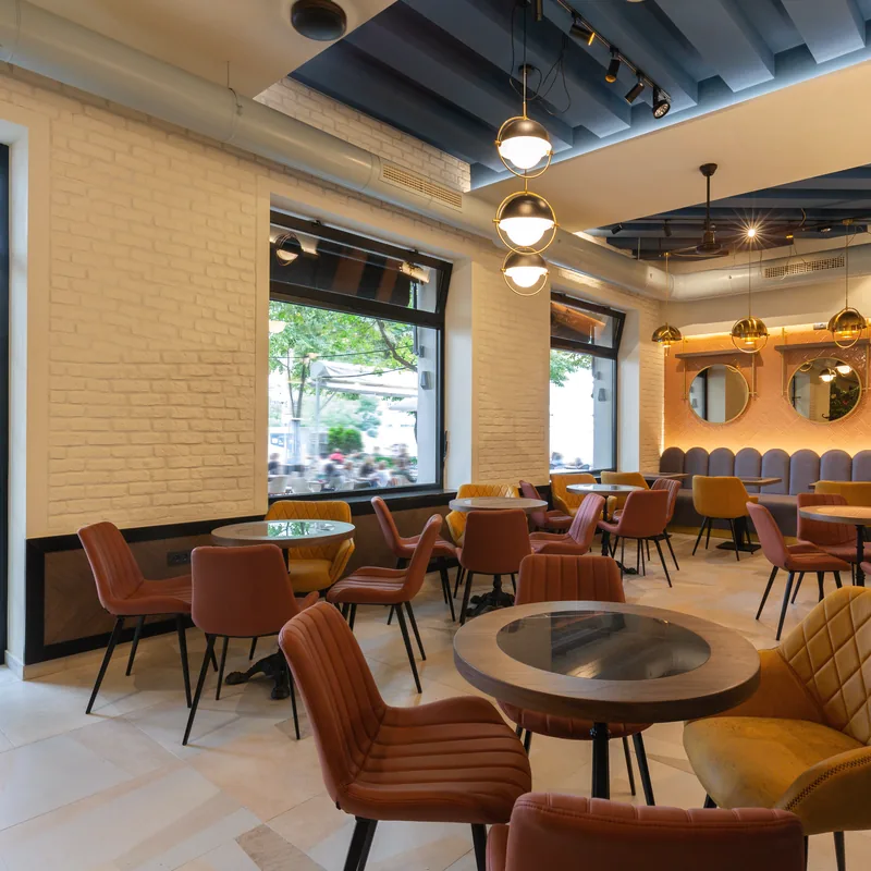 A cafe dining room with wooden tables, tan leather chairs and tall windows.