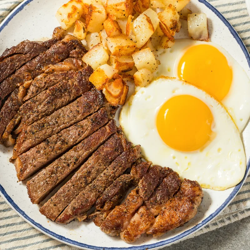 Sliced steak with two fried eggs and roast potatoes on a rimmed plate.