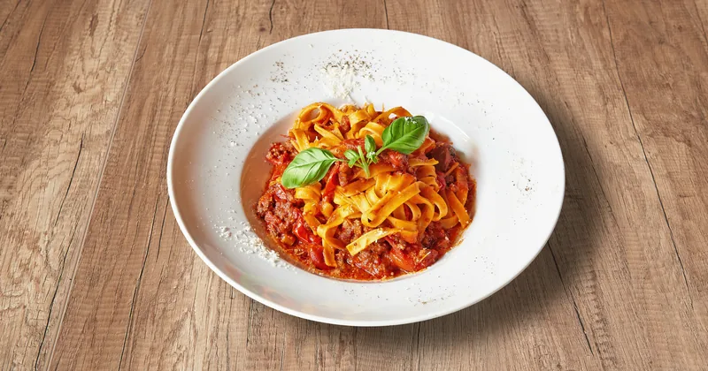 A plate of ribbon pasta in tomato sauce with basil, on a wooden table.