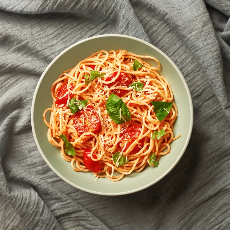 Spaghetti with cherry tomatoes and fresh basil in a shallow bowl.