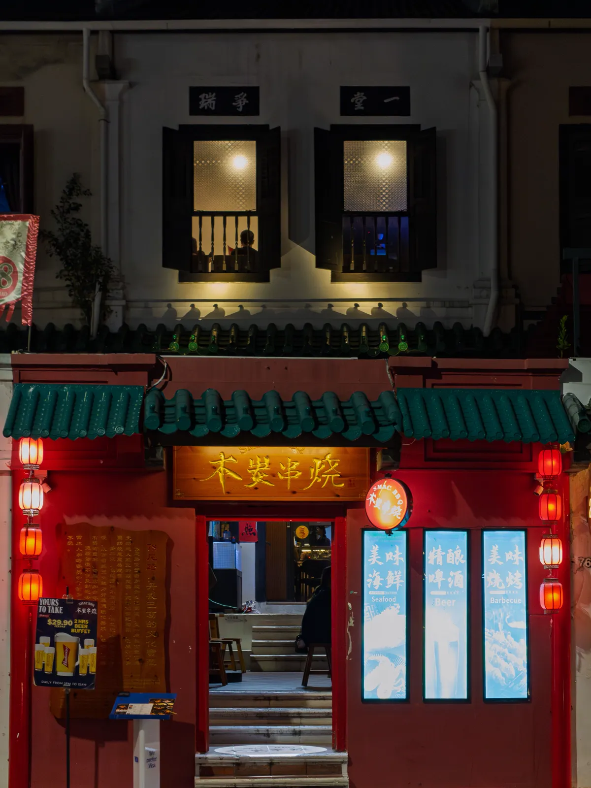 A red Chinatown shopfront at night, lanterns lit, the door open onto warm stairs.