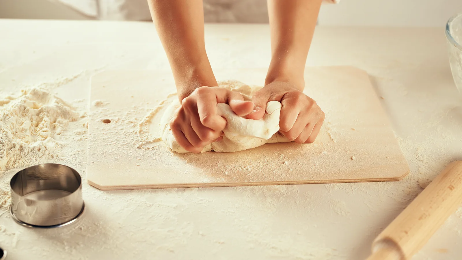 A pair of hands working a round of dough on a floured board.