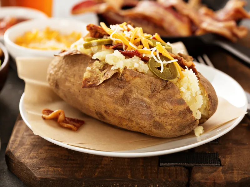 A baked potato split open and loaded with cheese and toppings on a white plate.