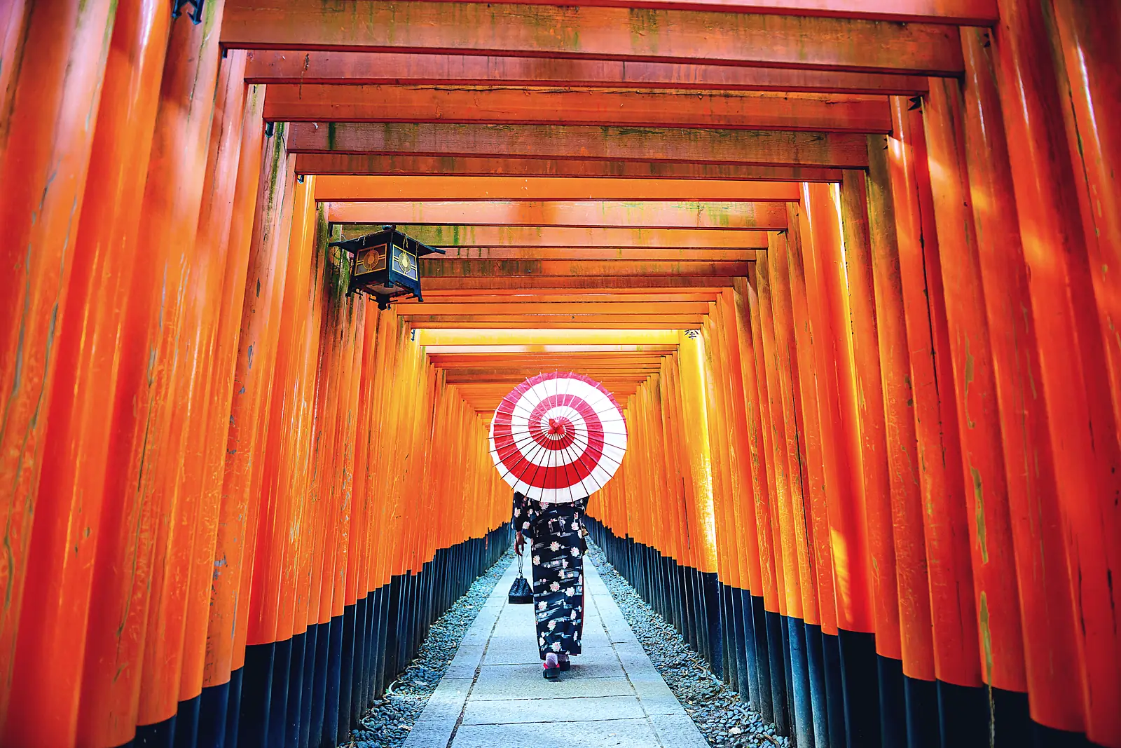 A woman with a red paper umbrella walking through the Senbon Torii at Fushimi Inari