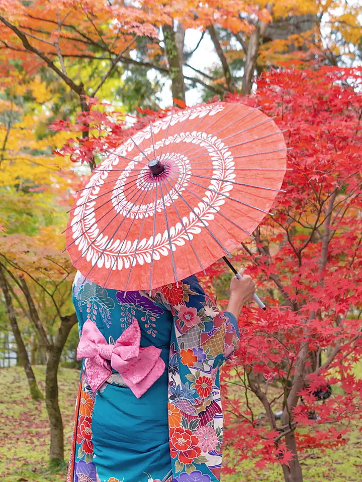 A woman in kimono under a red paper umbrella beneath scarlet maples in Kyoto
